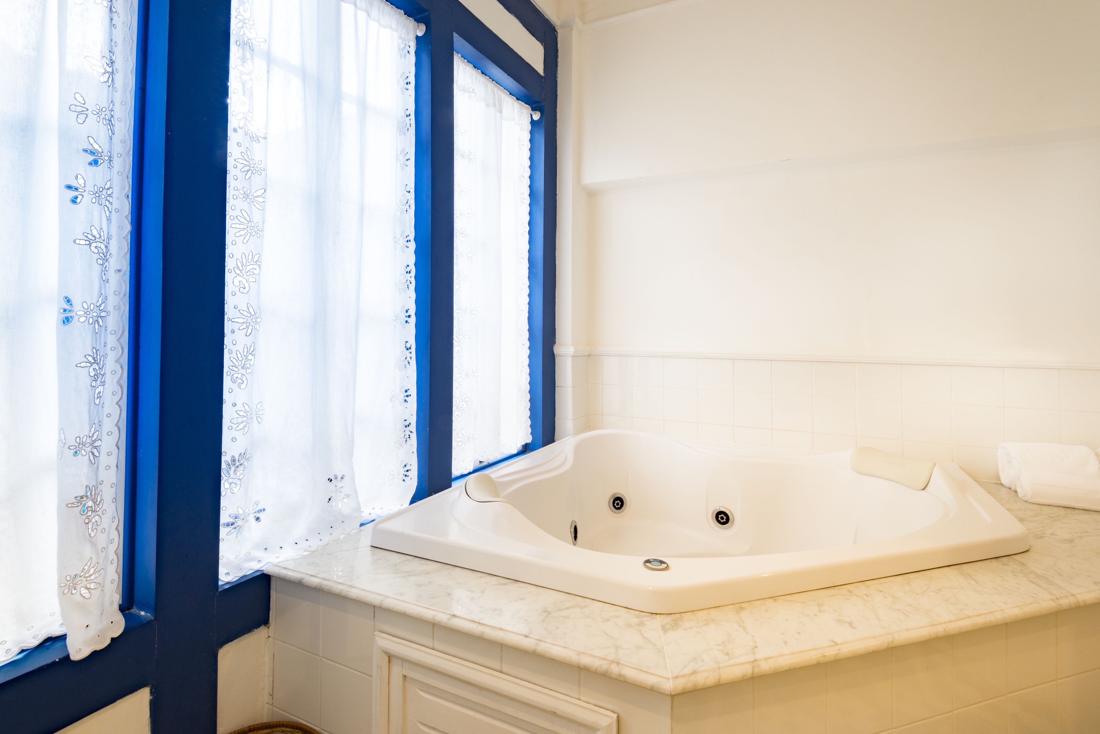 A bathroom with a white bathtub, blue window frames, and a white tiled wall.