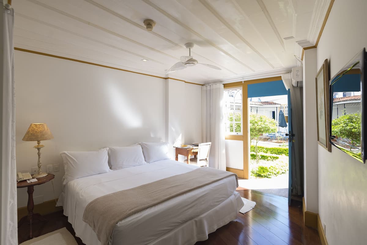 Un dormitorio con una cama grande, un ventilador de techo, una mesita de noche con lámpara y vistas al exterior.