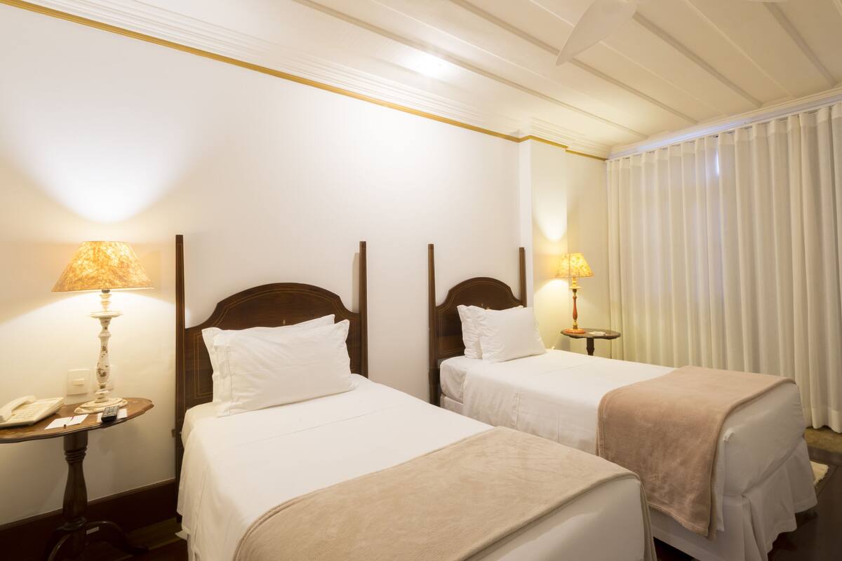 Habitación de hotel con dos camas individuales, una mesita de noche con lámpara, teléfono y espejo.