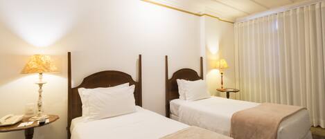 A hotel room with two single beds, a bedside table with a lamp, a telephone, and a mirror.