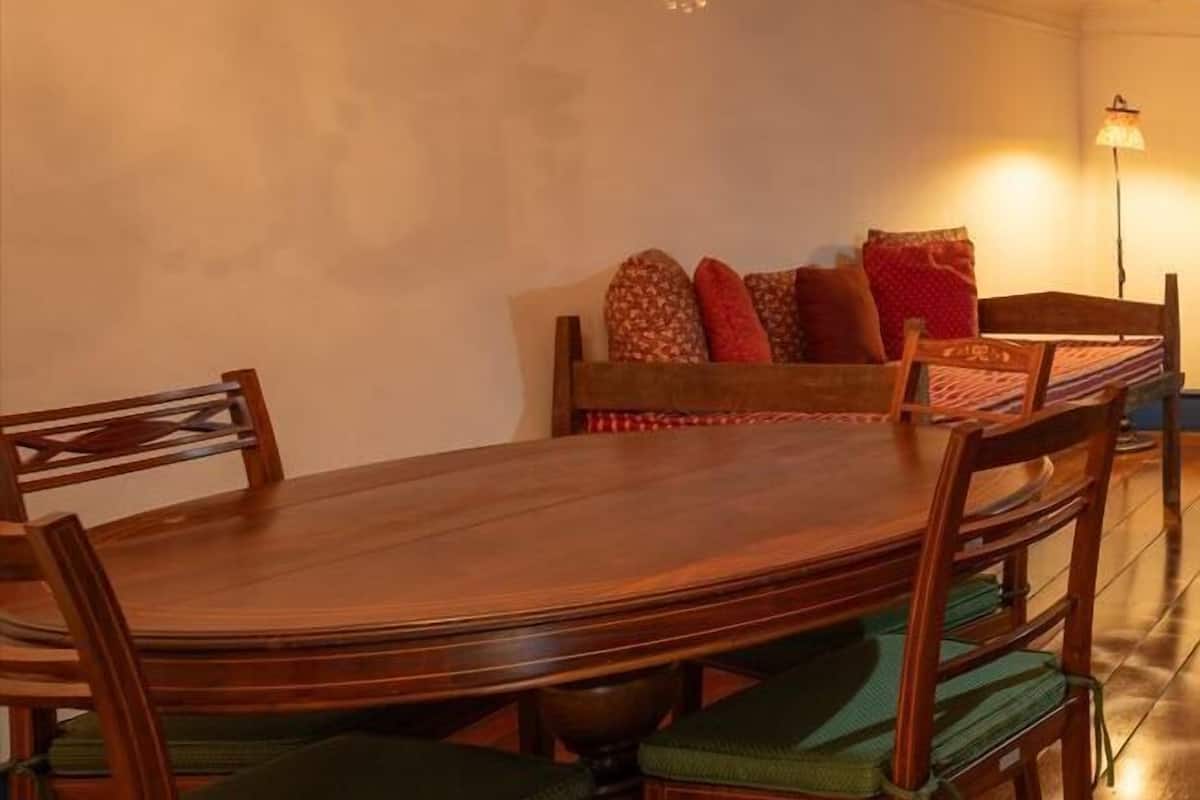 Un comedor con mesa y sillas de madera, una araña y un sofá con cojines.