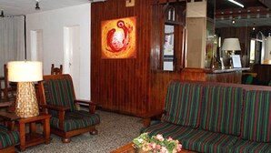 Ein Zimmer mit Holzwand, einer Couch, zwei Stühlen, einem Tisch mit Lampe und einem Gemälde.