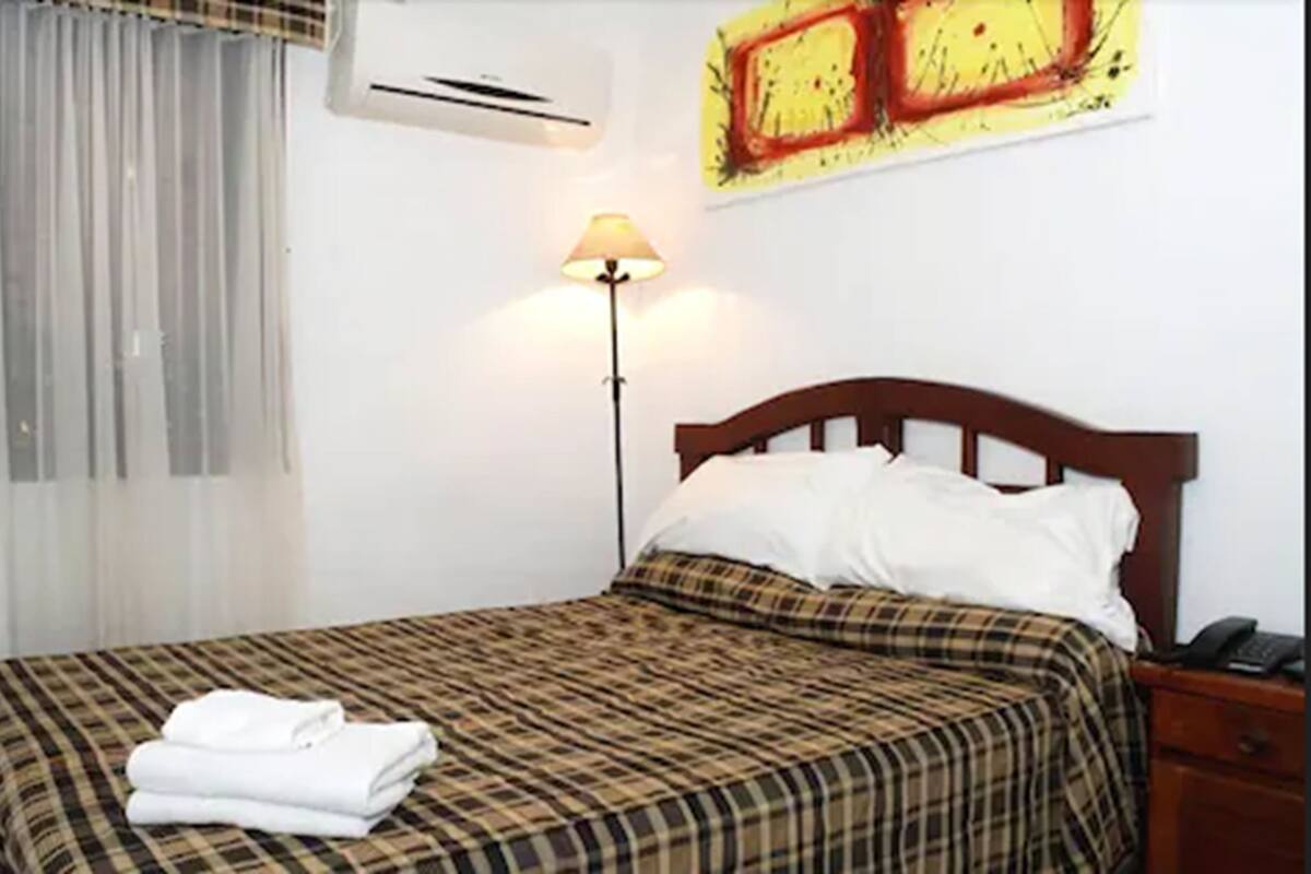 Habitación de hotel con cama, lámpara, mesita de noche y equipo de aire acondicionado.