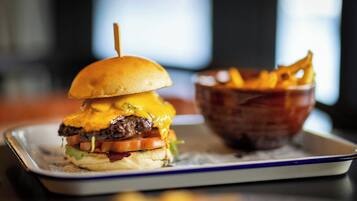 A burger with a toasted bun, cheese, lettuce, tomato, and a beef patty, served on a rectangular plate with a side of fries.