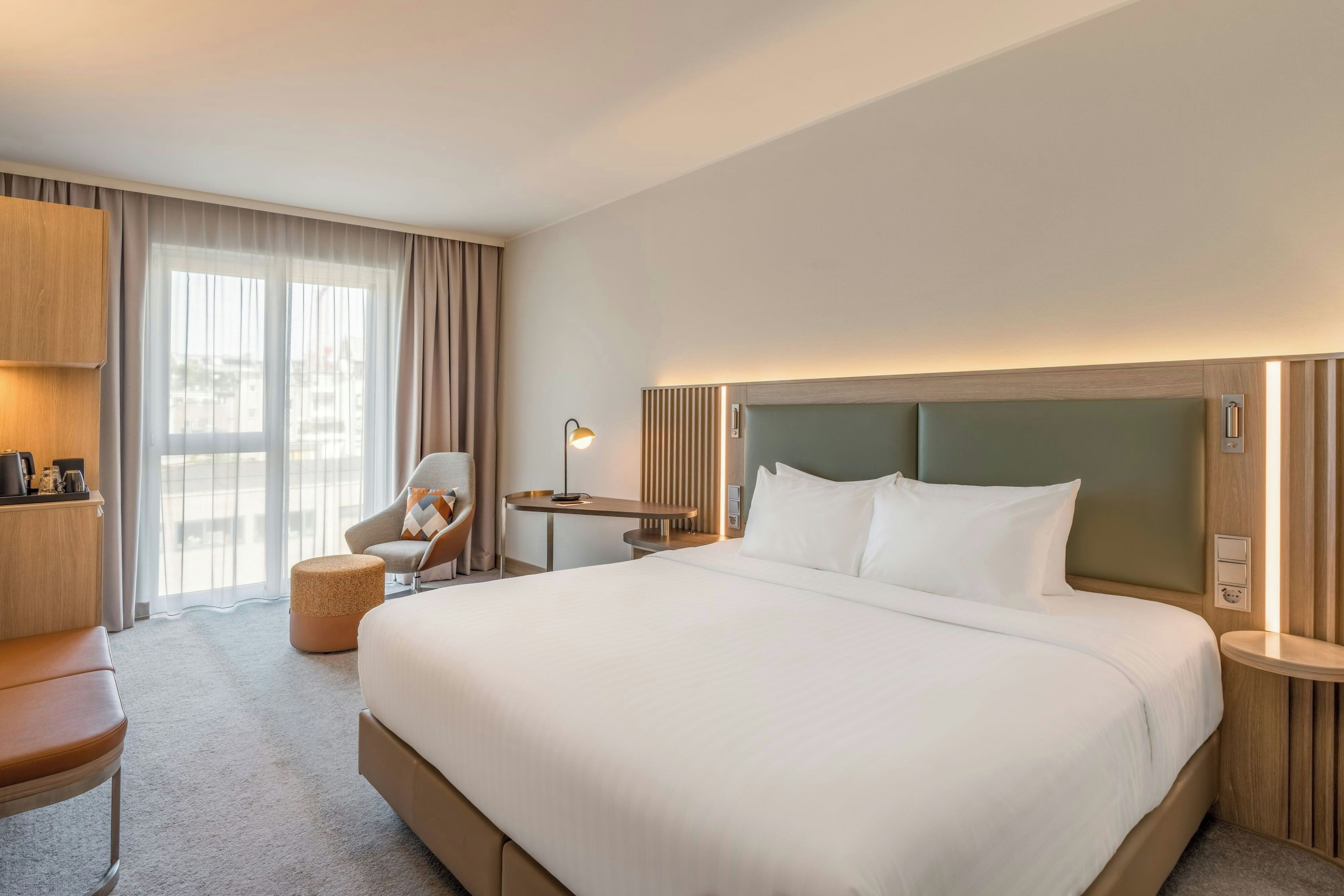 Habitación de hotel con una cama grande, un escritorio, una silla y vistas a la ciudad desde la ventana.