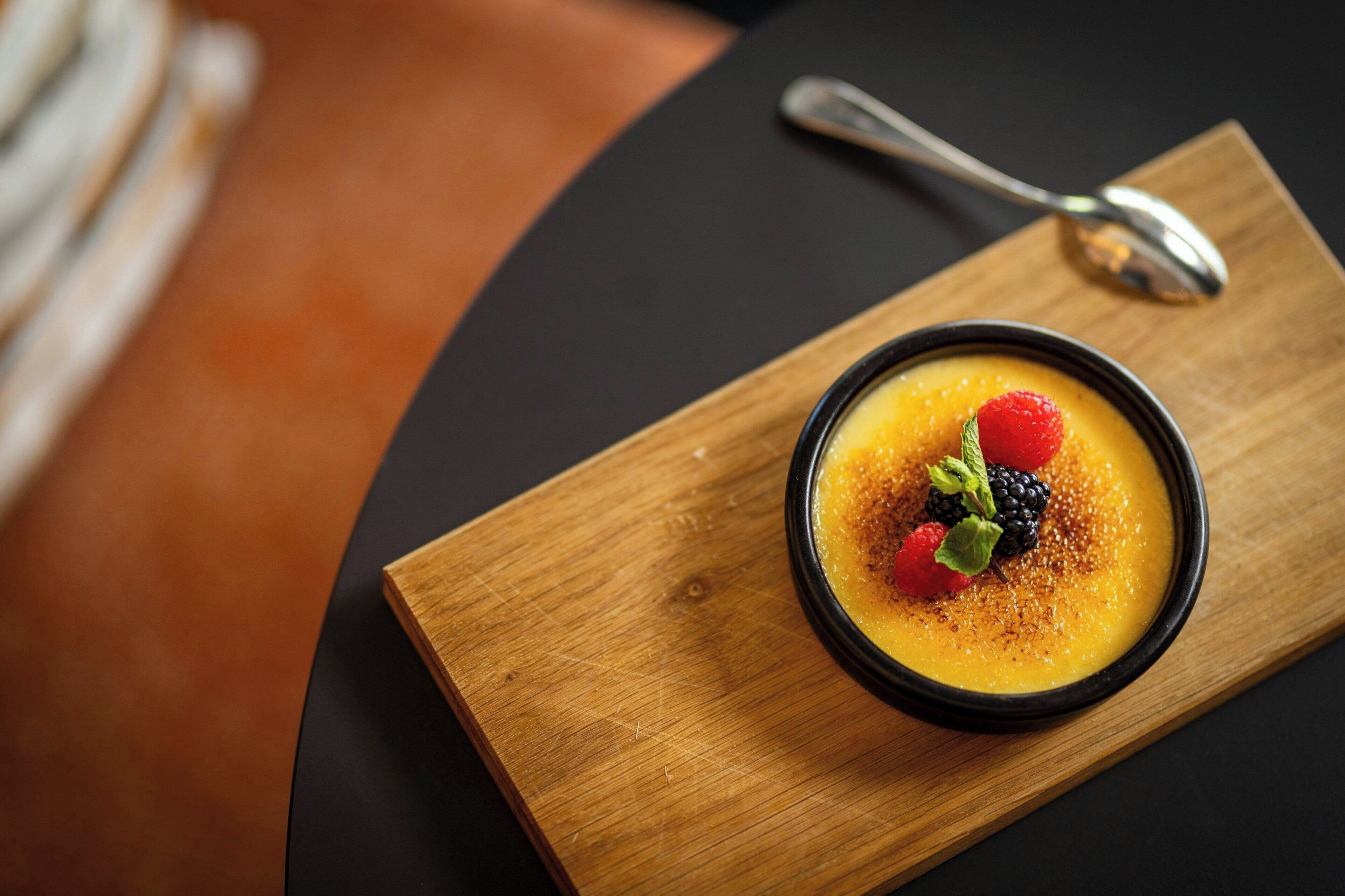 A dessert in a black bowl on a wooden board with a spoon beside it.