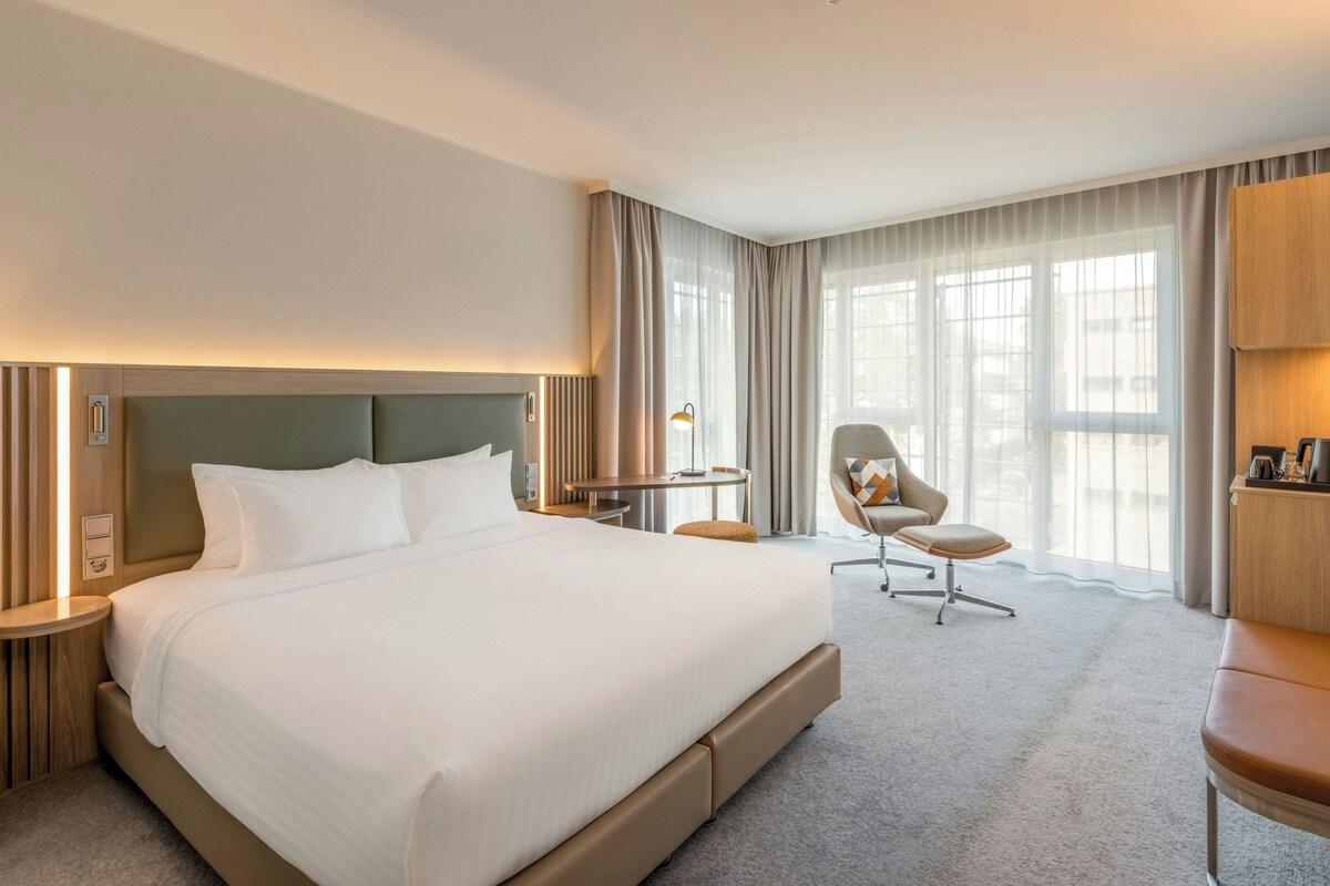 A hotel room with a large bed, a desk, a chair, and a wardrobe.