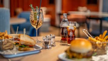 A dining table with a sandwich, fries, a burger, a glass of iced drink with a straw, and a bottle of cola.