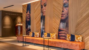 Een moderne lobby met een lange oranje bank, twee ronde tafels en een groot muurschilderij.