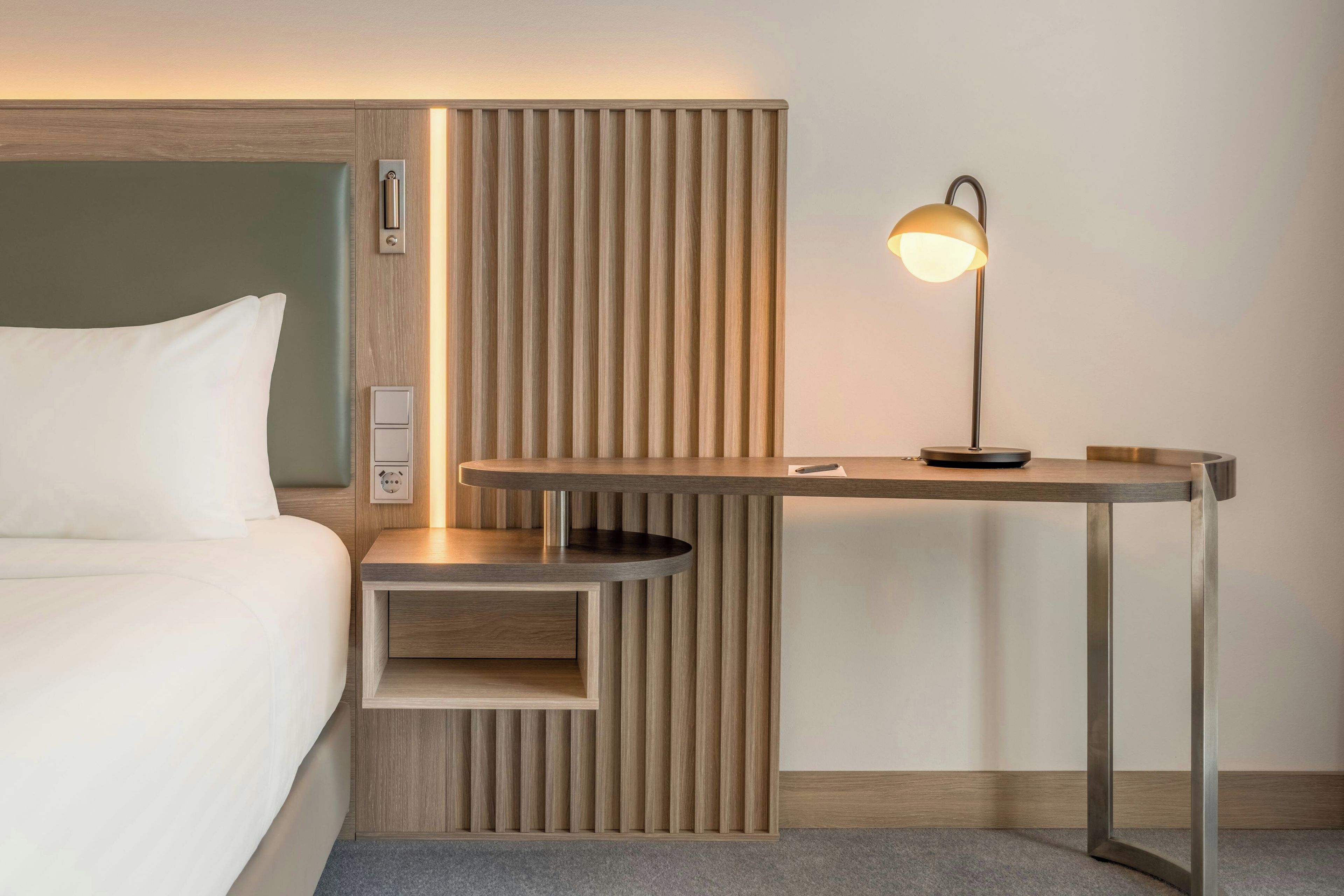 A hotel room with a bed, a bedside table with a lamp, and a built-in shelf.