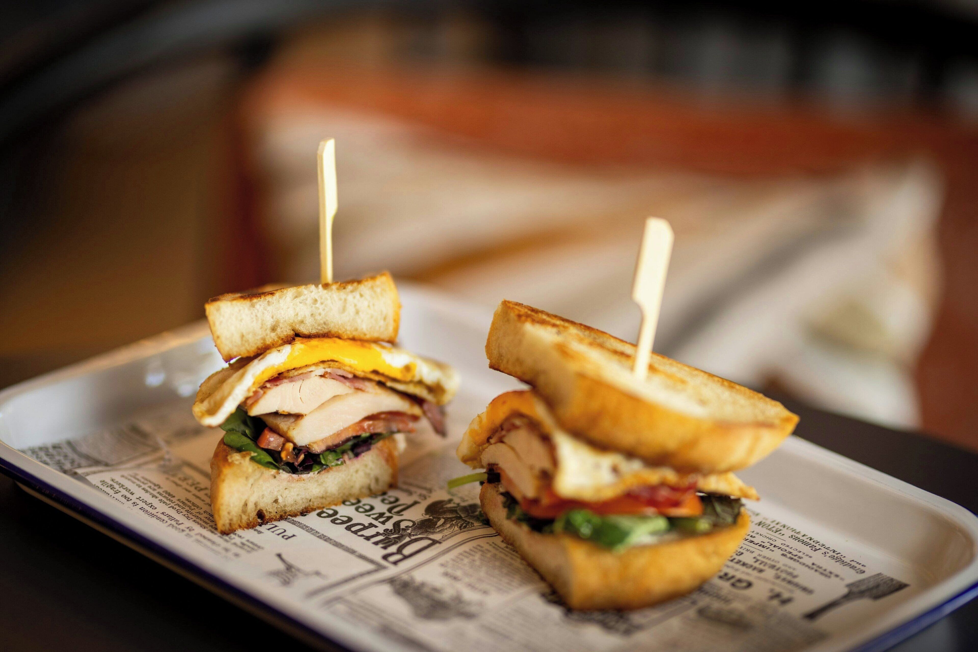 Two grilled sandwiches on a plate with a newspaper underneath.