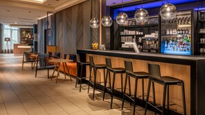 Een moderne bar met een lange toonbank, barstoelen en een goed gevulde drankendisplay.