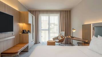 Una habitación de hotel con cama, escritorio, silla, televisor y ventana con cortinas.