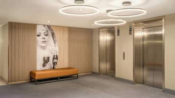 A modern elevator area with a bench, wall-mounted elevators, and circular ceiling lights.