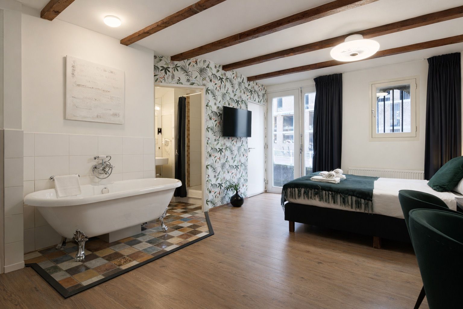 Een kamer met een badkuip, een bed, een televisie en een raam met gordijnen.