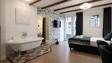Una habitación con bañera, cama, televisor y ventana con cortinas.