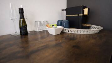 Una mesa de madera con una botella de vino, copas, un bol blanco con aperitivos y una bandeja decorativa.