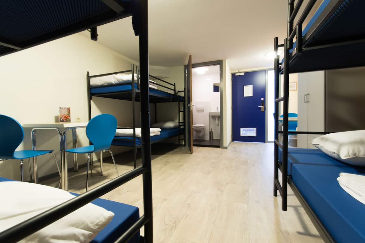 Un dormitorio con literas, escritorio, sillas y baño.