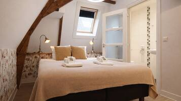 A bedroom with a bed, pillows, a nightstand, a window, and a door.