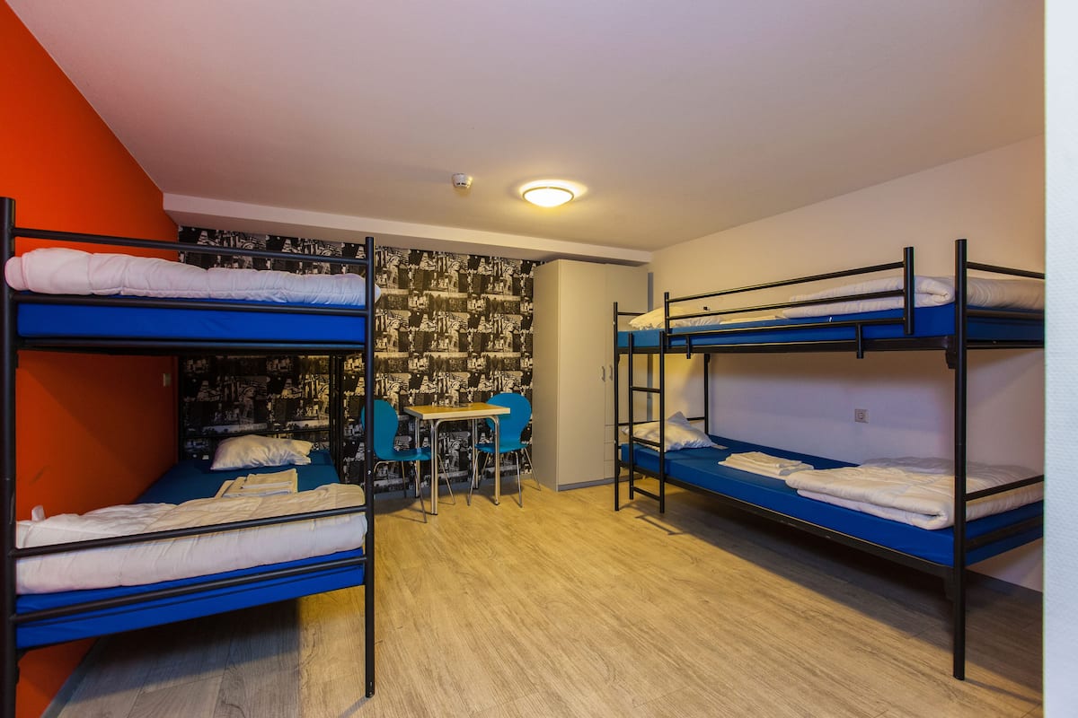 Un dormitorio con literas, una mesita pequeña y sillas azules.