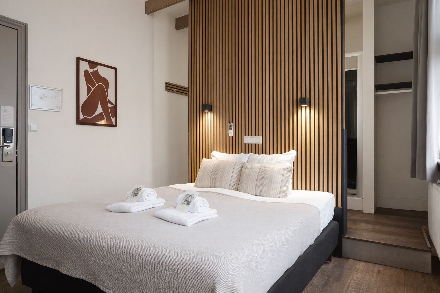 A hotel room with a bed, towels, a wall-mounted artwork, and a wooden panel wall.