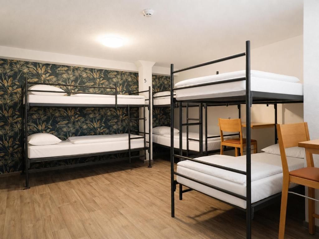A dormitory room with bunk beds, a wooden chair, and a small table.
