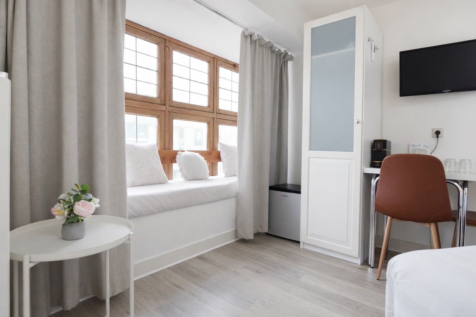 Una habitación de hotel con cama, escritorio con silla, televisión y ventana con cortinas.