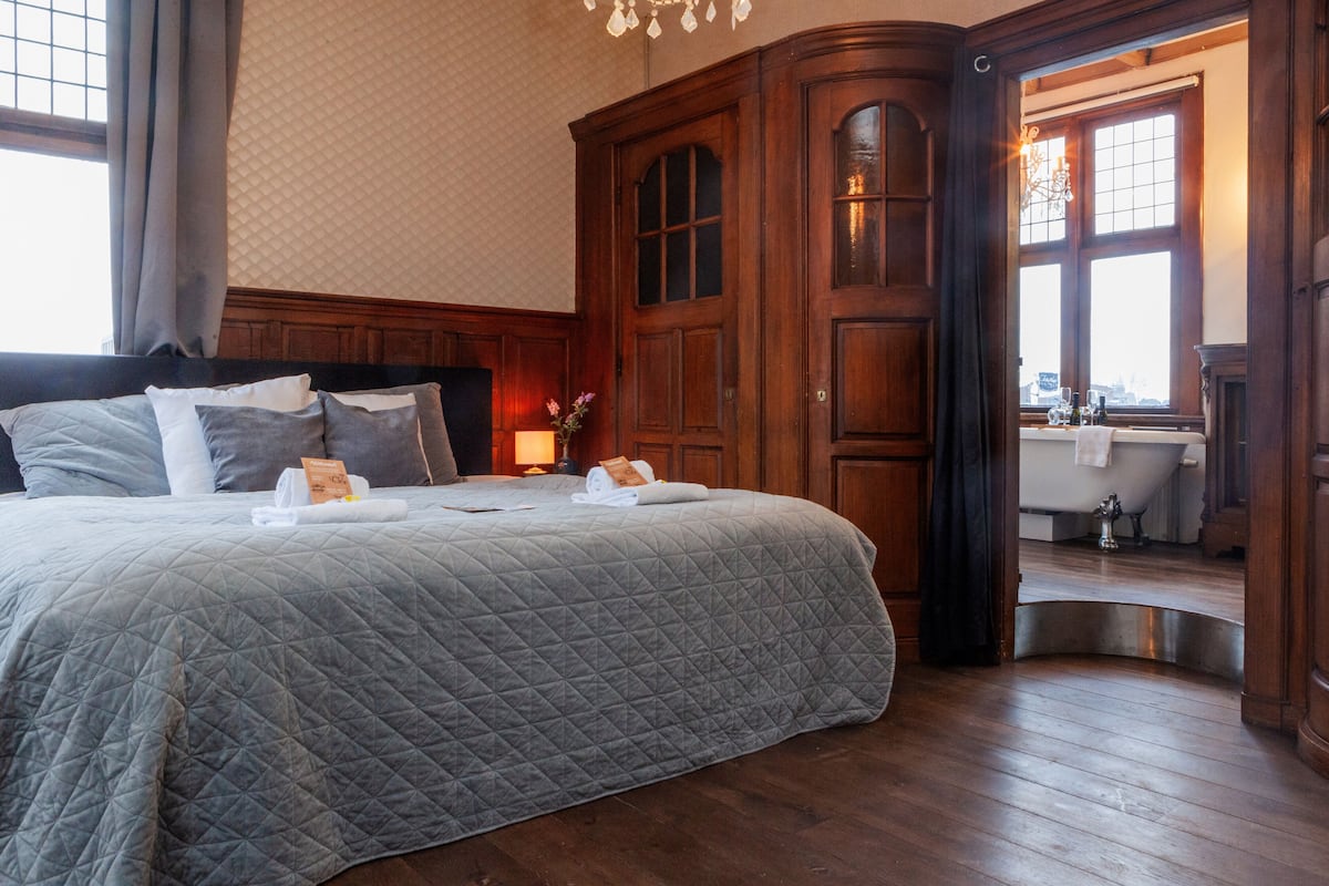 Habitación de hotel con una cama grande, armario de madera y vistas al baño.