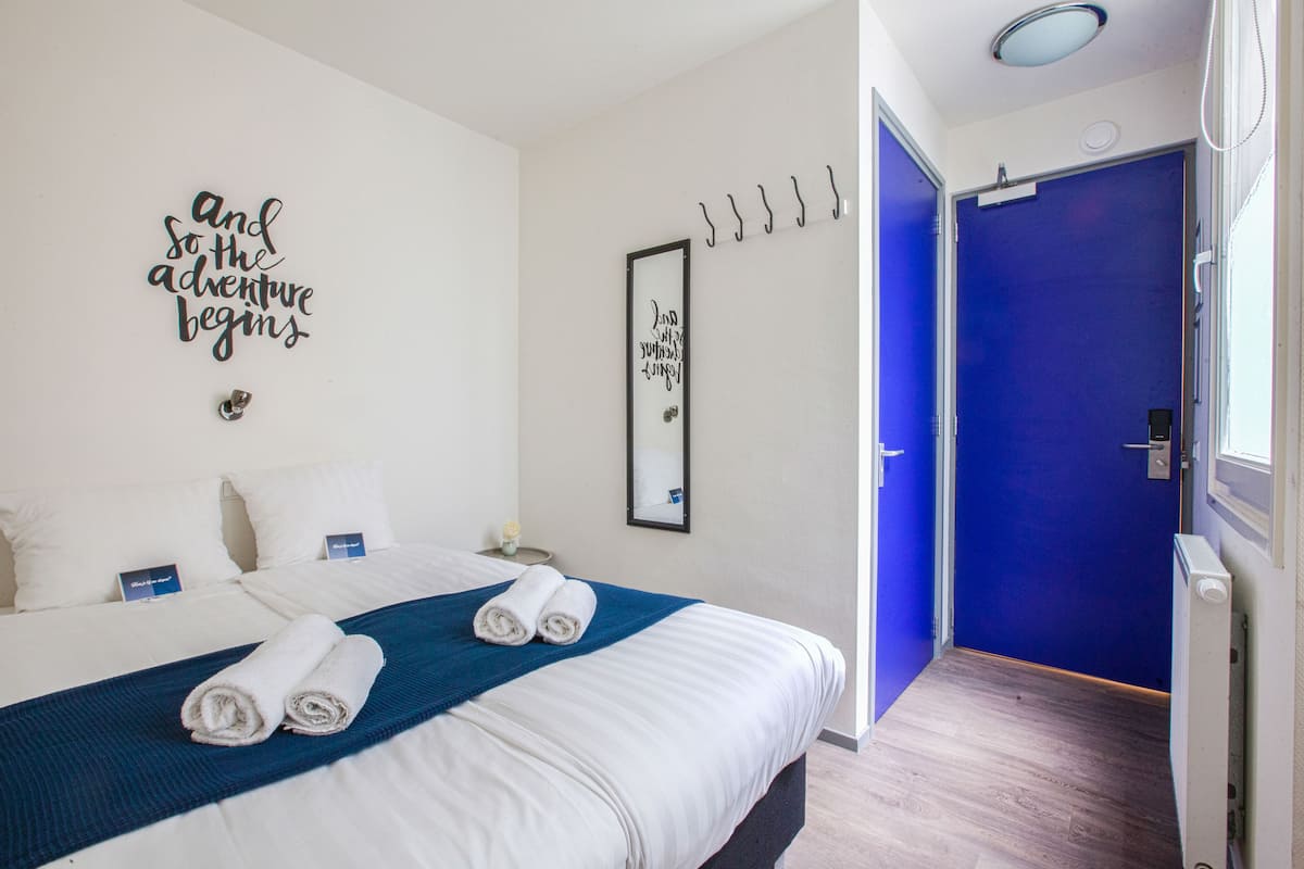 Una habitación de hotel con una cama, una puerta azul y una pared con citas motivacionales.