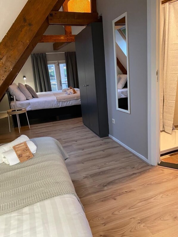 A bedroom with a lofted sleeping area, wooden beams, a bed with pillows, a nightstand, and a window with curtains.