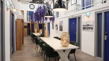 A modern interior with a long dining table, green chairs, hanging purple flowers, and a staircase.
