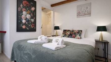 A hotel room with a bed, two bedside lamps, a painting, and a bathroom visible through an open door.