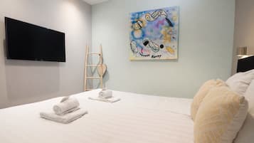 A hotel room with a bed, towels, a painting, a television, and a ladder.
