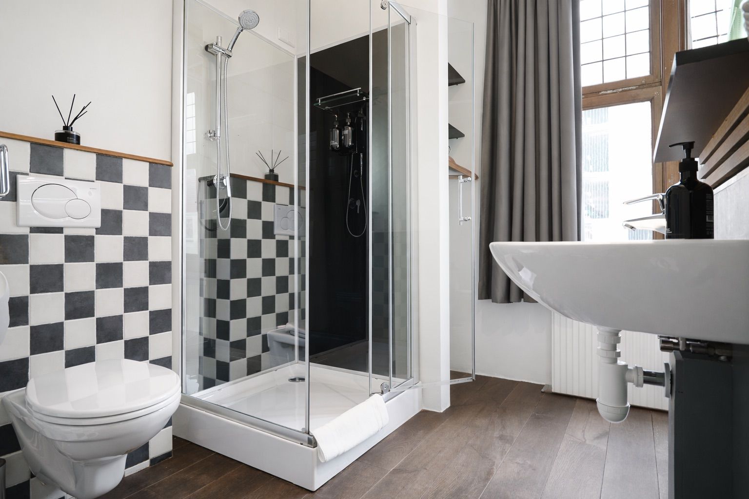 Une salle de bain moderne avec une douche à parois de verre, des toilettes blanches et un lavabo équipé d’un distributeur de savon.