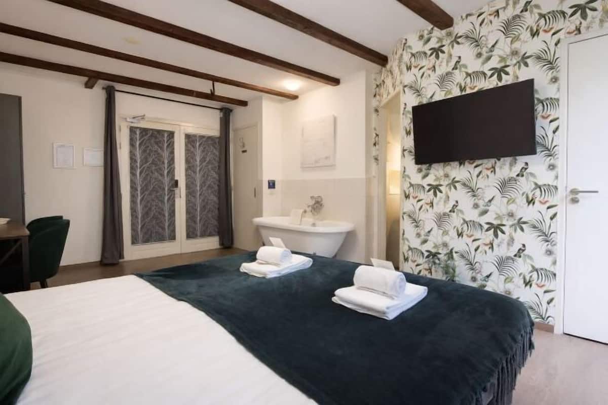 Habitación de hotel con cama, escritorio, silla, lavamanos y televisión.
