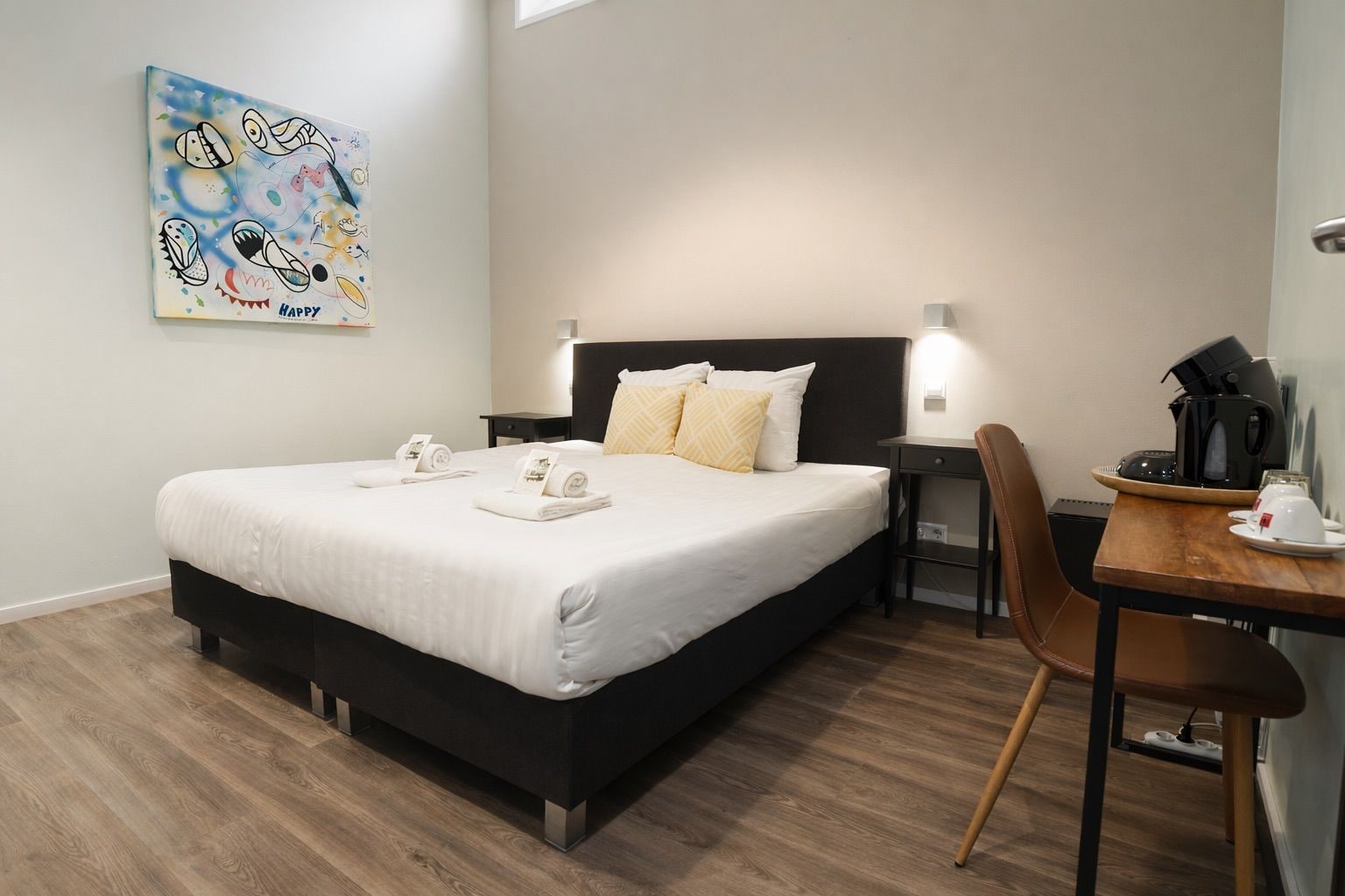 Una habitación de hotel con cama, mesita de noche, silla y un cuadro en la pared.