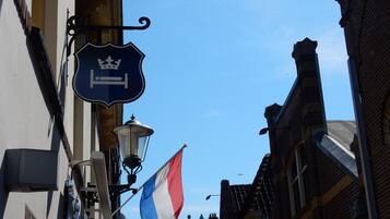 A narrow street with buildings on either side, a street lamp, and a flag.