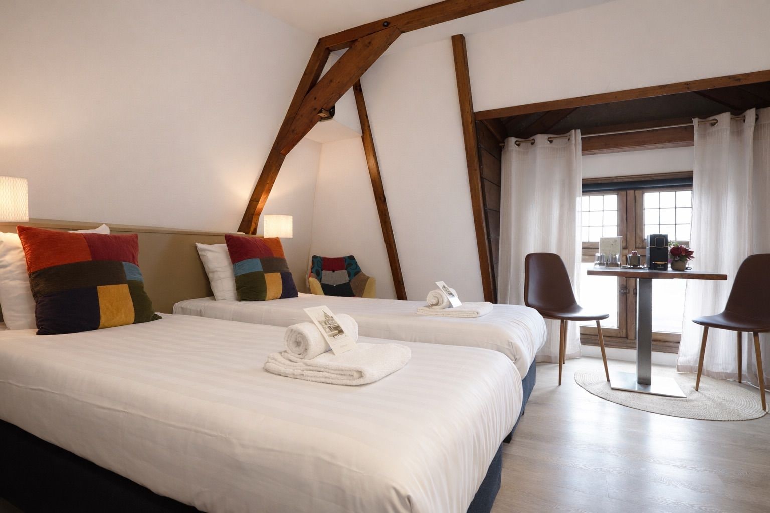 A hotel room with two beds, a small table with chairs, and a window with curtains.