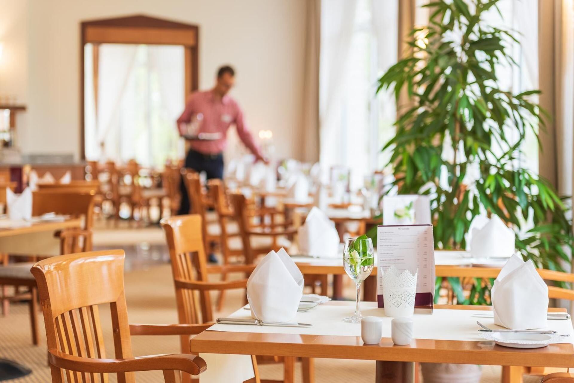 A restaurant setting with wooden tables and chairs, white table settings, and a menu.