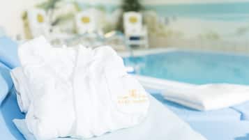 A white towel with embroidered text on a hotel bed with a pool in the background.