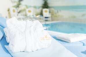 A white towel with embroidered text on a hotel bed with a pool in the background. - Bel Air Strandhotel (Glowe)