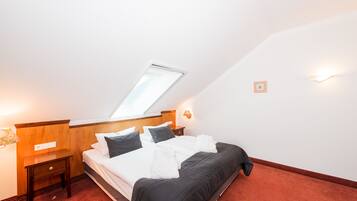 A neatly made bed in a room with a sloped ceiling, a small bedside table, and a wall-mounted light fixture.