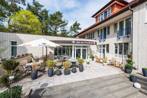 An outdoor patio area with tables and chairs, potted plants, and a sign for Bel Air Strandhotel. - Bel Air Strandhotel (Glowe)