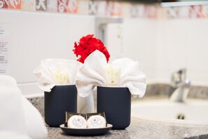 A bathroom with a sink, a mirror, and a towel rack holding two white towels and a red flower. - Bel Air Strandhotel (Glowe)