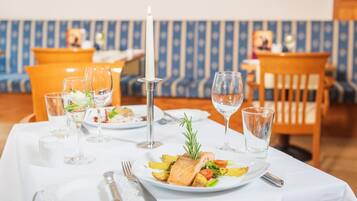 A dining table set with plates of food, glasses, cutlery, and a candle.