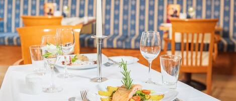 A dining table set with plates of food, glasses, cutlery, and a candle.