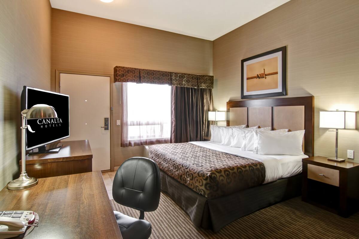 Habitación de hotel con cama, mesita de noche, lámpara, escritorio con teléfono y televisión.