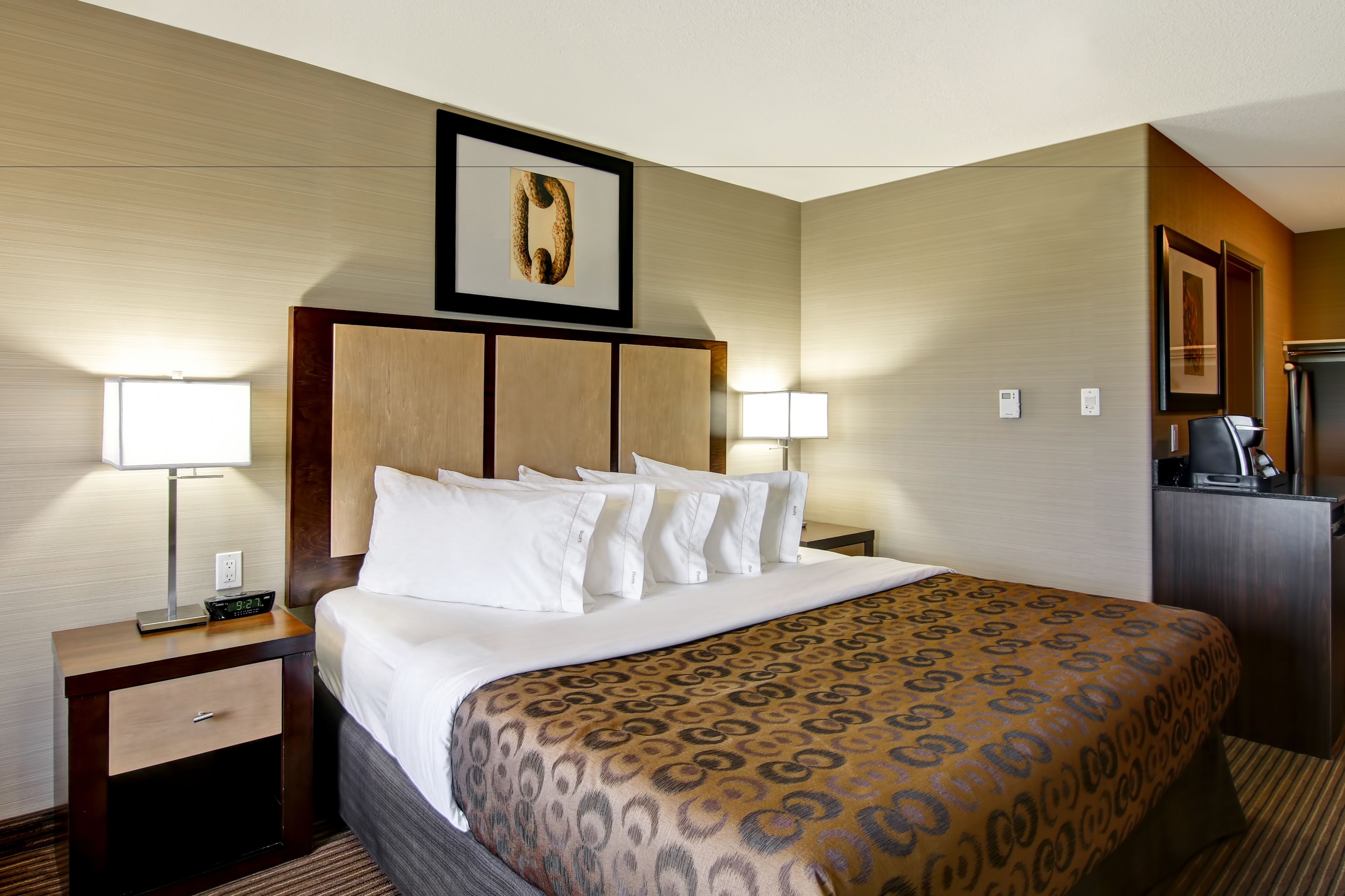 A hotel room with a large bed, a nightstand with a lamp, a wooden headboard, and a framed picture on the wall.