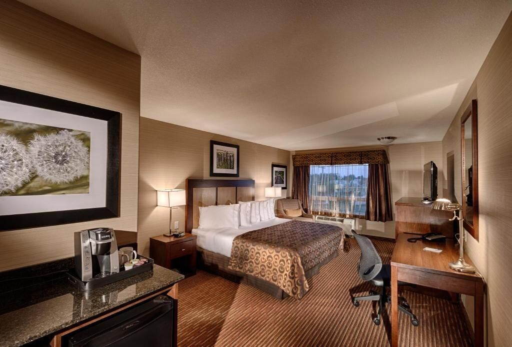 A hotel room with a bed, desk, chair, coffee maker, and a view of the city through the window.