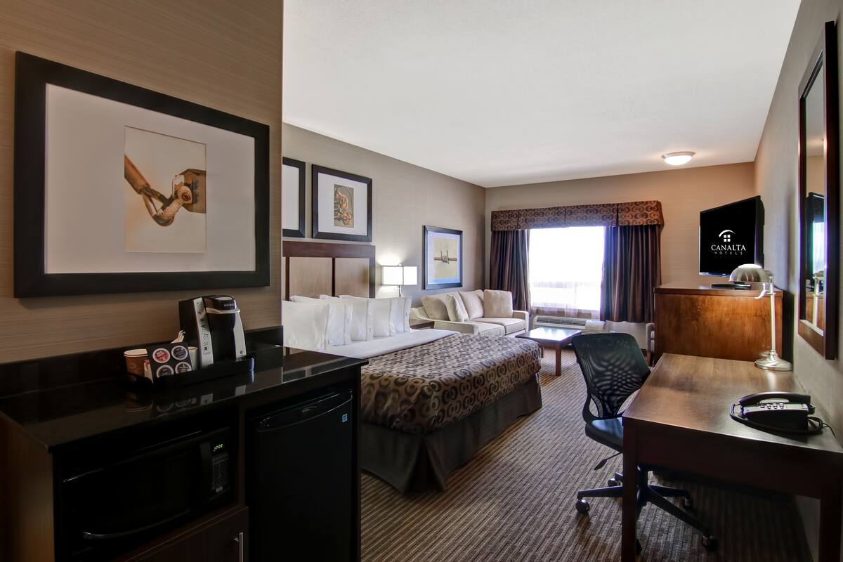 Habitación de hotel con cama, escritorio, silla, cafetera, microondas y televisión.
